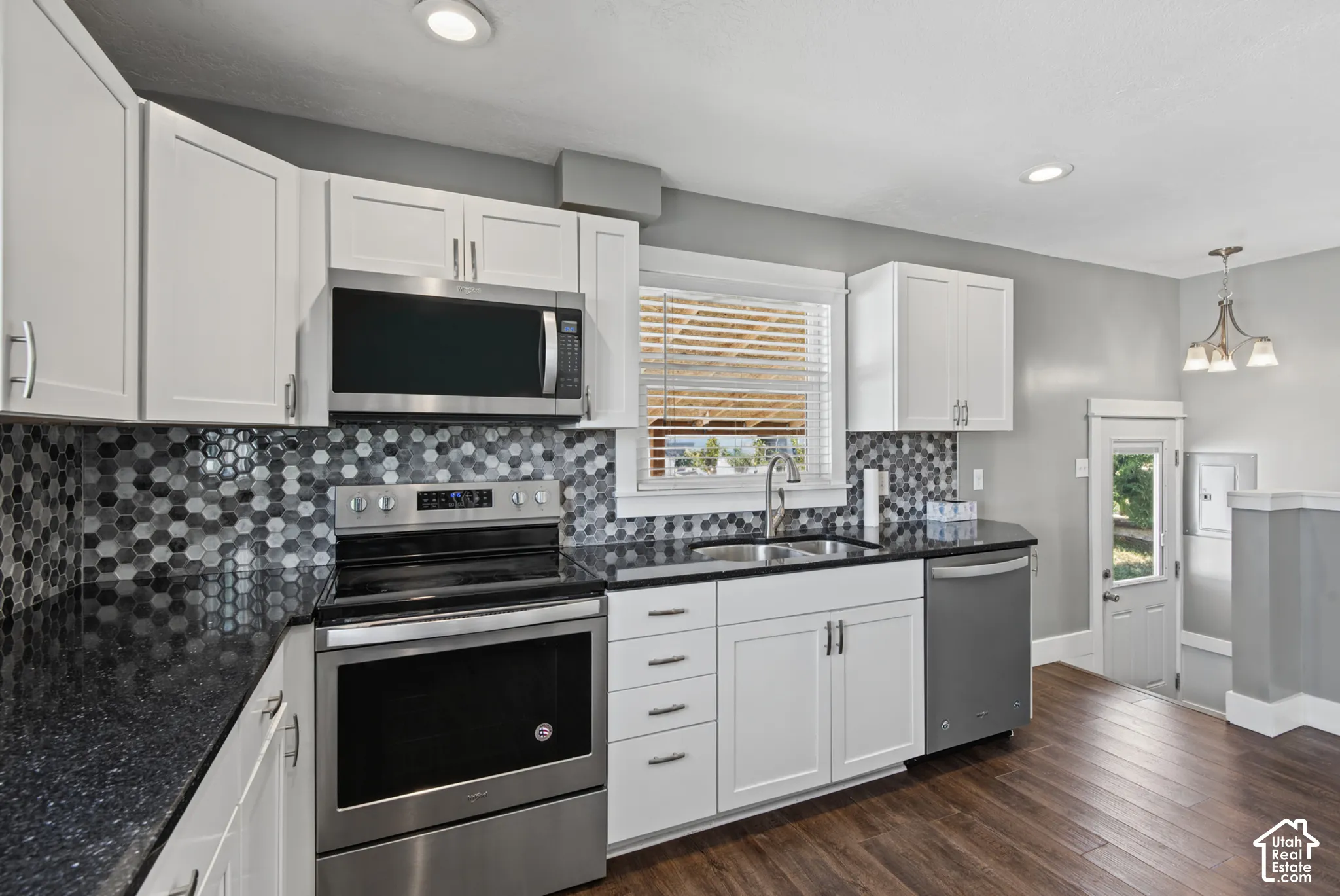 White cabinetry, stainless steel appliances, dark speckled countertops, mosaic tile backsplash, and wood-finish flooring