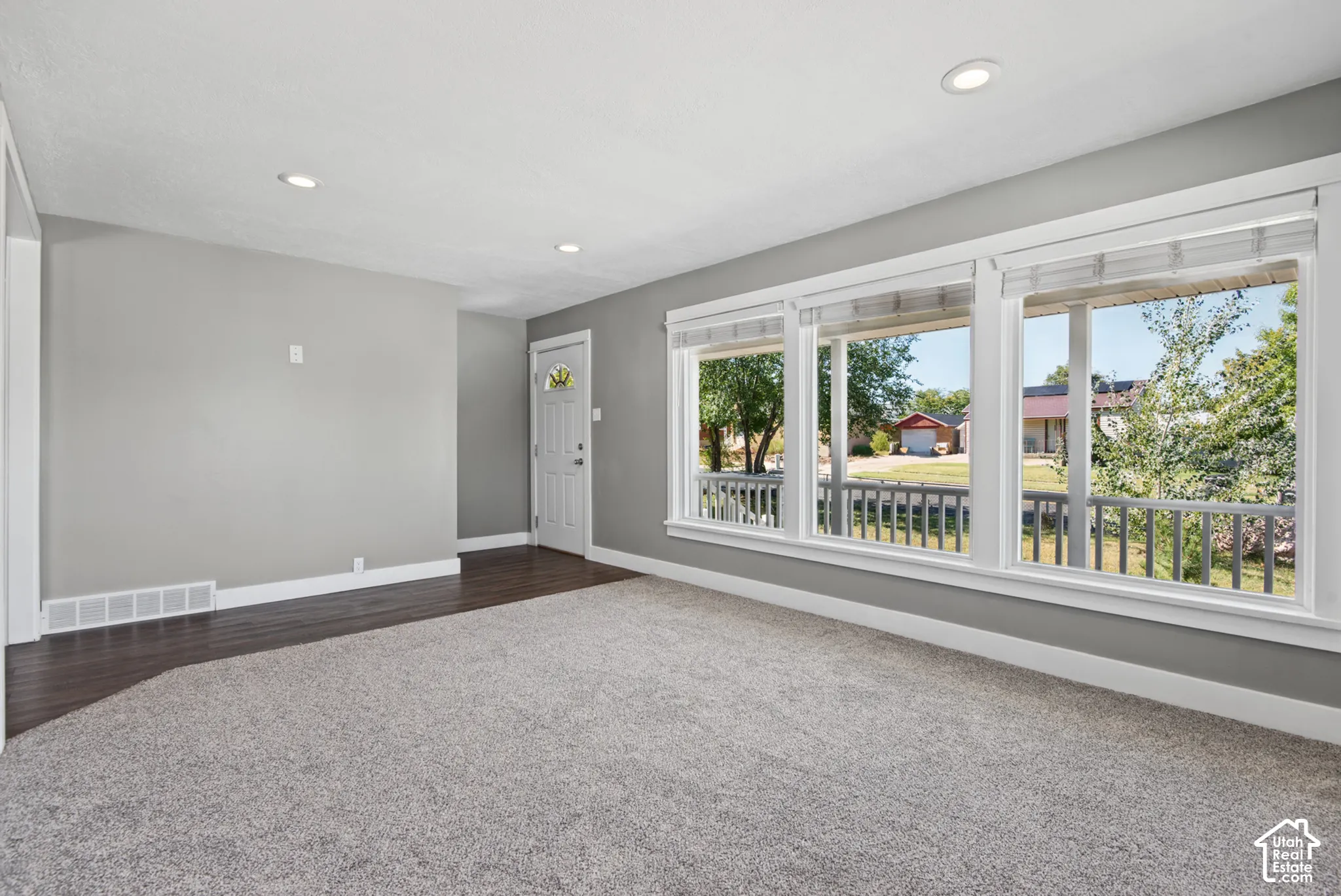 Light gray wall paint, recessed ceiling lighting, dark wood-finish flooring, light gray carpet, and a white entry door