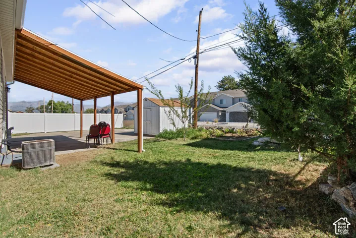 Expansive backyard featuring a covered patio, concrete pad, storage shed, and mature landscaping