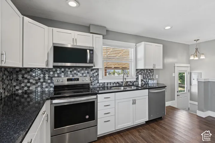 White cabinetry, stainless steel appliances, dark speckled countertops, mosaic tile backsplash, and wood-finish flooring