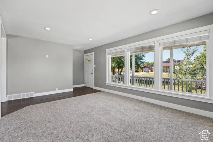 Light gray wall paint, recessed ceiling lighting, dark wood-finish flooring, light gray carpet, and a white entry door