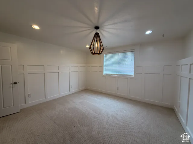 Board and batten wainscoting, recessed lighting, and a contemporary geometric pendant light illuminate this carpeted room with a single window