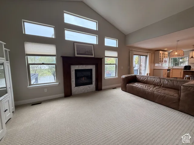 Vaulted ceiling with multiple windows, gas fireplace featuring a wood surround and tile hearth, and plush carpeting