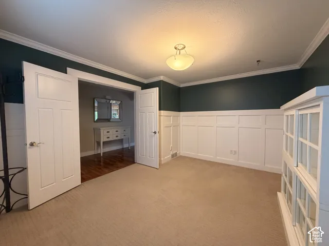 Carpeted room featuring elegant wainscoting and crown molding, with a semi-flush mount ceiling fixture providing illumination