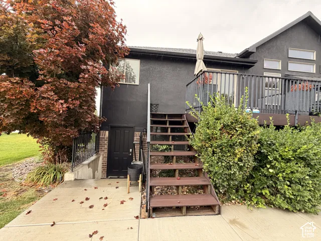 Exterior featuring dark stucco siding, a brick-faced entryway, and an elevated deck with dark railings