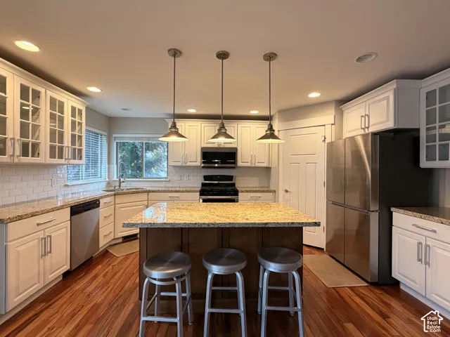 Kitchen featuring wood-finish flooring, white cabinetry, a central island with a stone countertop, stainless steel appliances, and subway tile backsplash