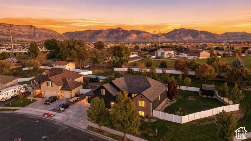 Aerial perspective of a detached residential property featuring dark-toned exterior siding, a multi-gabled asphalt shingle roof, concrete driveway, and a white privacy fence surrounding the rear yard