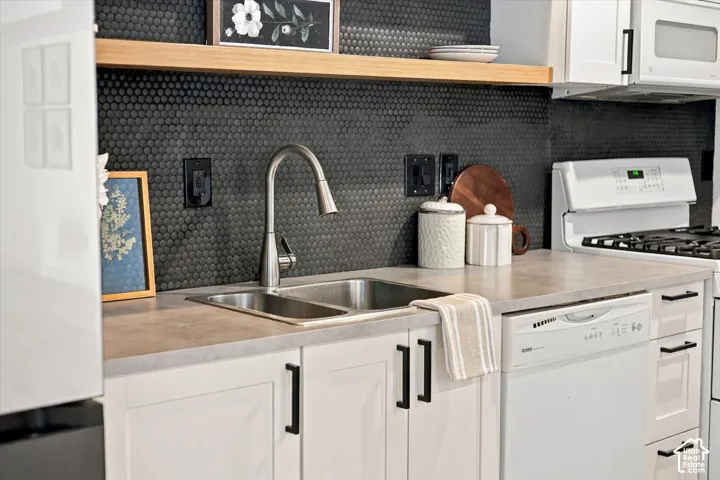 Kitchen area featuring white shaker-style cabinetry with matte black hardware, a black penny-round tile backsplash, light-toned countertops, a stainless steel dual-basin undermount sink with a gooseneck faucet, and natural wood-finish open shelving