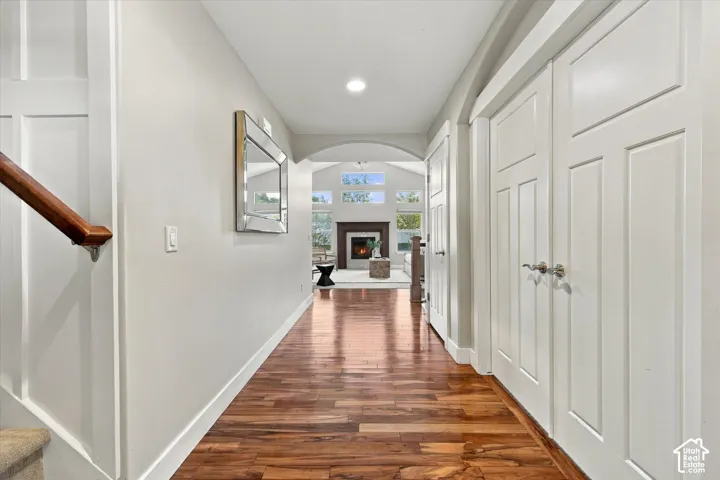 Entryway featuring wood-finish flooring, an arched ceiling detail, double-panel doors, and a fireplace with a vaulted ceiling and stacked window configuration