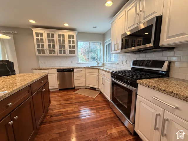 Kitchen featuring wood-finish flooring, white cabinetry, granite countertops, and stainless steel appliances