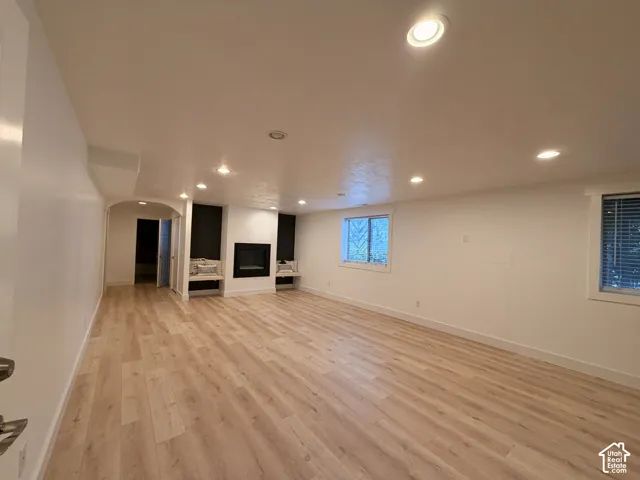 Spacious room featuring wood-finish flooring, a contemporary fireplace, built-in shelving, recessed lighting, and multiple windows