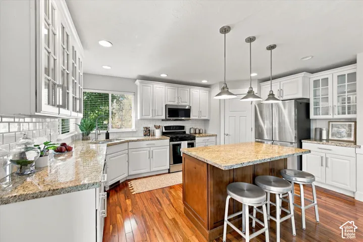 Kitchen featuring white cabinetry with glass-front uppers, stone countertops, a central island with a wood base, stainless steel appliances, and wood-finish flooring