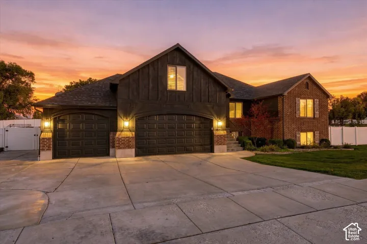 Multi-level exterior featuring brick and board-and-batten siding, a three-car garage, concrete driveway, and expansive lawn
