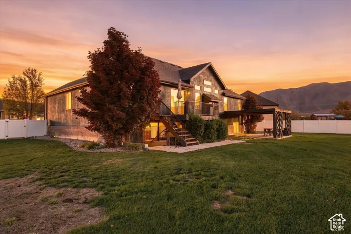 Multi-level residence featuring stone and siding exterior, elevated deck with metal railing, covered pergola patio, and white vinyl perimeter fencing set against a mountain backdrop