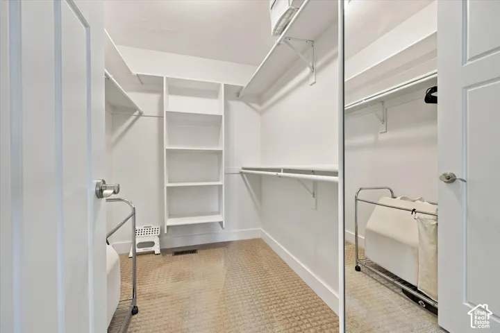 Walk-in closet featuring white built-in shelving, full-length mirrored closet doors, and wall-to-wall carpeting
