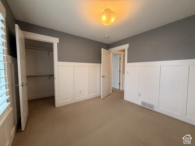 Carpeted room with wainscoting, solid panel doors, overhead lighting, and built-in closet shelving