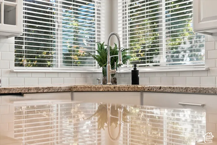 Kitchen area featuring stone-surface countertops, white subway tile backsplash, dual windows with horizontal blinds, and a gooseneck pull-down faucet