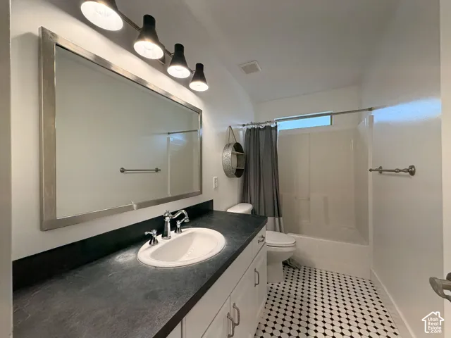 Black and white hexagonal tile flooring, white vanity with polished chrome hardware, dark countertop, framed mirror, and a white tub with shower