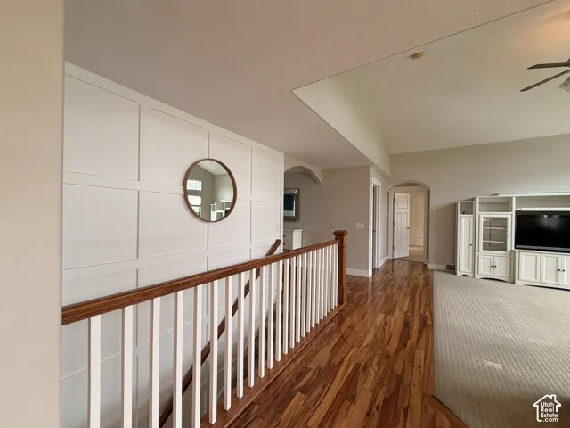 Wood-finish flooring, white panel wall detailing, vaulted ceiling, built-in entertainment center, and archway architectural elements