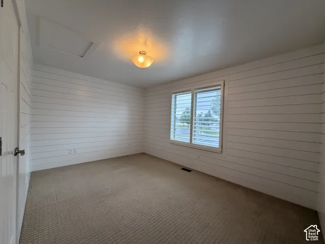 White shiplap accent wall, carpeted flooring, window with white plantation shutters, white ceiling, and a ceiling-mounted light fixture