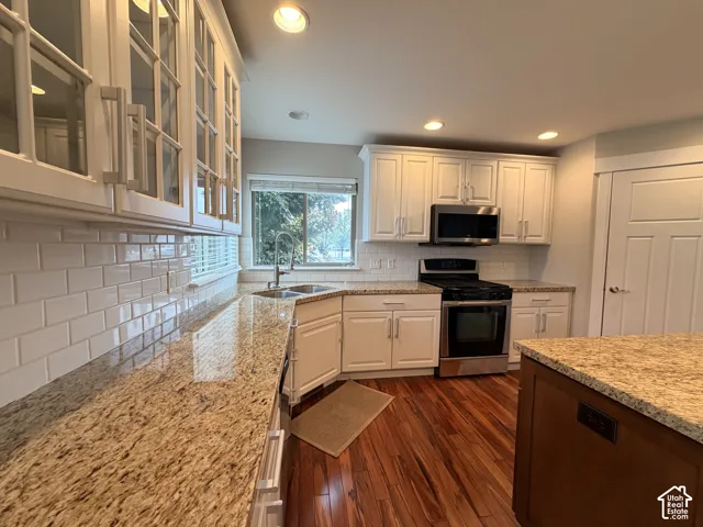 White shaker cabinetry, granite countertops, stainless steel appliances, wood-finish flooring, and white subway tile backsplash