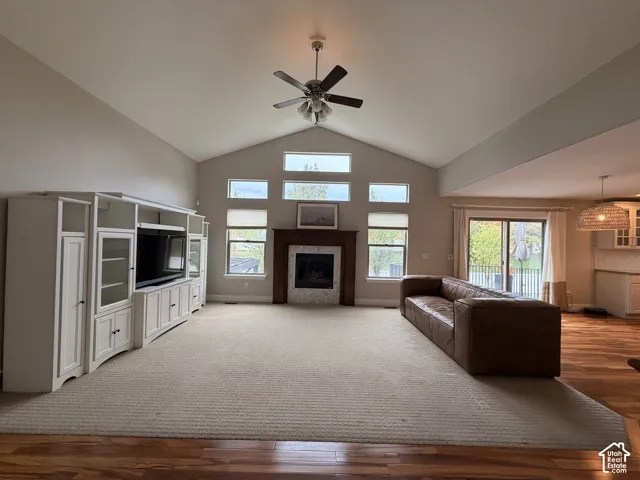 Vaulted ceiling with a ceiling fan, a built-in media console, a fireplace with a wood mantel, multiple windows, and sliding glass doors