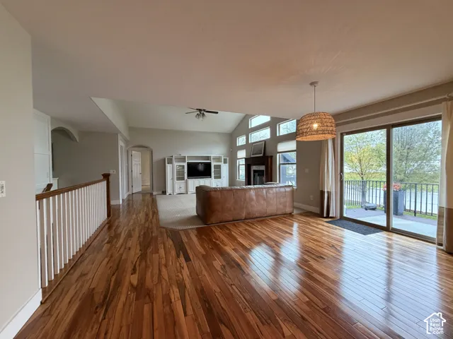 Hardwood flooring throughout, vaulted ceiling, built-in media console, ceiling fan, and sliding glass door with balcony access