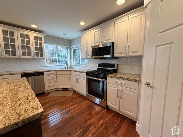 Kitchen featuring hardwood flooring, white shaker cabinetry, granite countertops, subway tile backsplash, and stainless steel appliances