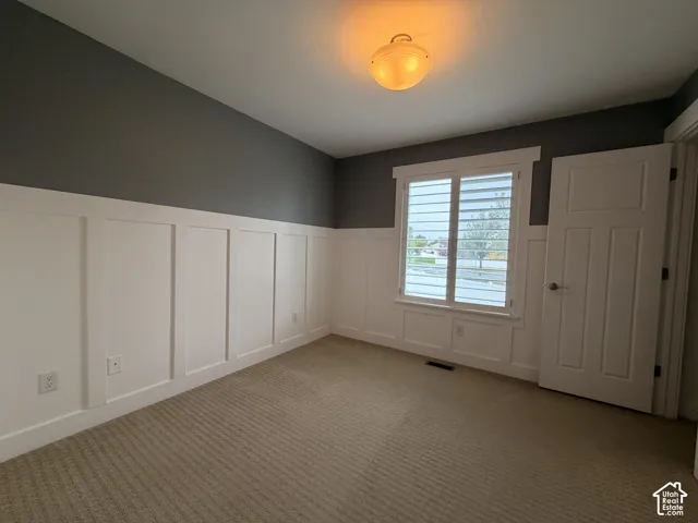 Board and batten wall detailing, neutral carpet, ceiling-mounted light fixture, window with plantation shutters, and a paneled interior door