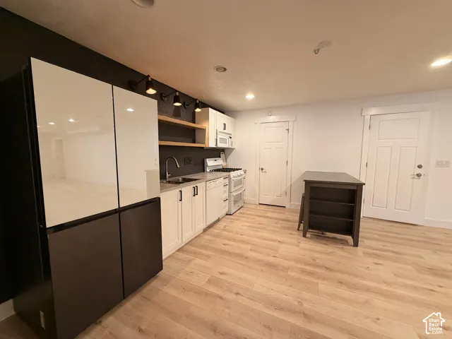 Wood-finish flooring throughout, full kitchen with white cabinetry and integrated appliances, and a modern refrigerator with a dark and light paneled finish