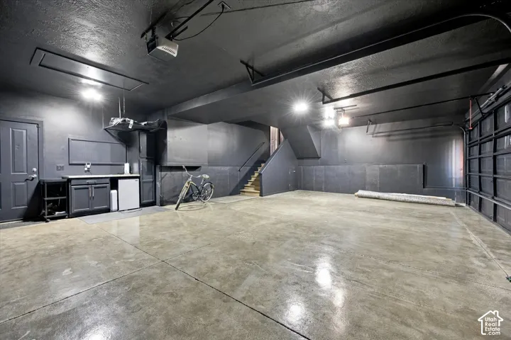 Multi-car garage featuring a polished concrete floor, built-in cabinetry with a countertop, recessed lighting, and a staircase