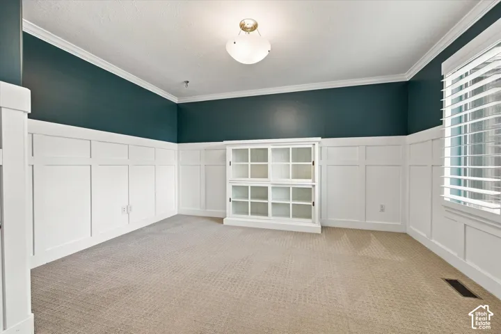 Room featuring crisp white wainscoting, built-in glass-front cabinetry, neutral wall-to-wall carpeting, crown molding, and a semi-flush mount ceiling fixture
