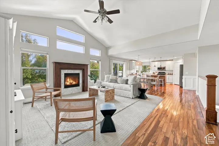 Vaulted ceilings featuring a central paddle fan, wood-finish flooring, and a fireplace with a wood mantel and tile surround