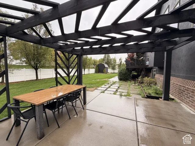 Patio area featuring a black pergola, concrete slab flooring, and a landscaped yard