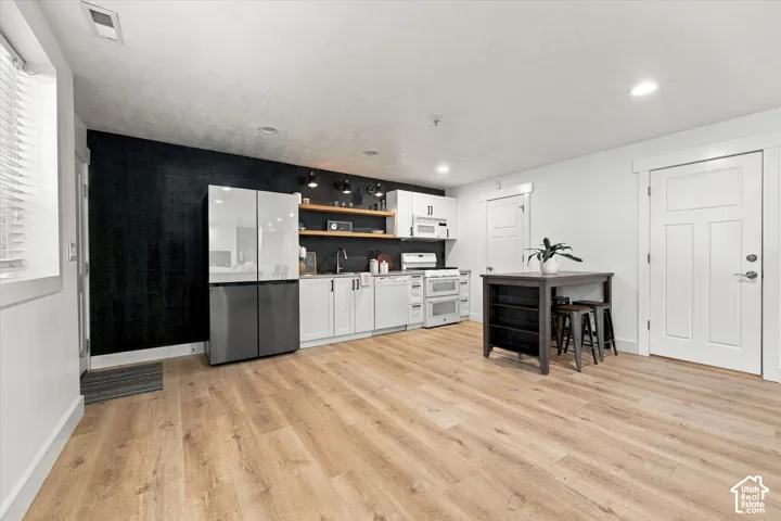 Kitchen featuring wood-finish flooring, white shaker-style cabinetry, open wood shelving, a dark accent wall, and recessed lighting