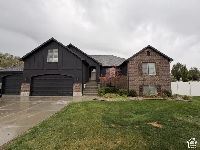 Brick and board-and-batten exterior, multi-car garage, concrete driveway, front entry steps, and a landscaped yard