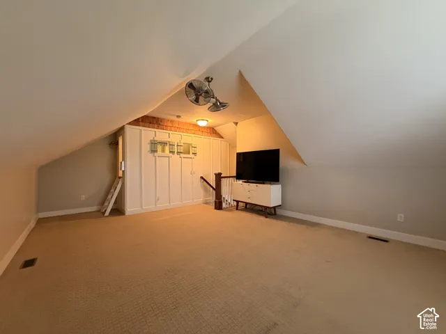 Spacious attic bedroom with vaulted ceilings, ceiling fan with integrated lighting, carpeted flooring, and built-in closet storage