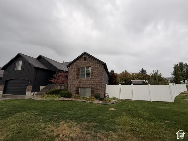 Brick and vertical siding exterior with an attached garage, pitched shingle roof, and a white privacy fence