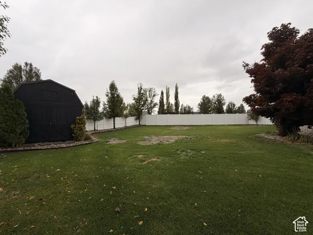Expansive yard featuring a white privacy fence, mature trees, and a black storage shed