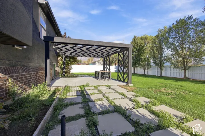 Backyard featuring a covered patio with a dark metal pergola, a concrete slab, a segmented stone paver path, and a perimeter fence