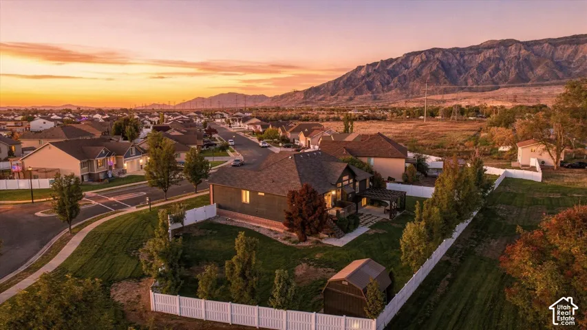 Aerial view of a residential property featuring a fenced backyard, mature trees, a detached storage shed, and a mountain backdrop