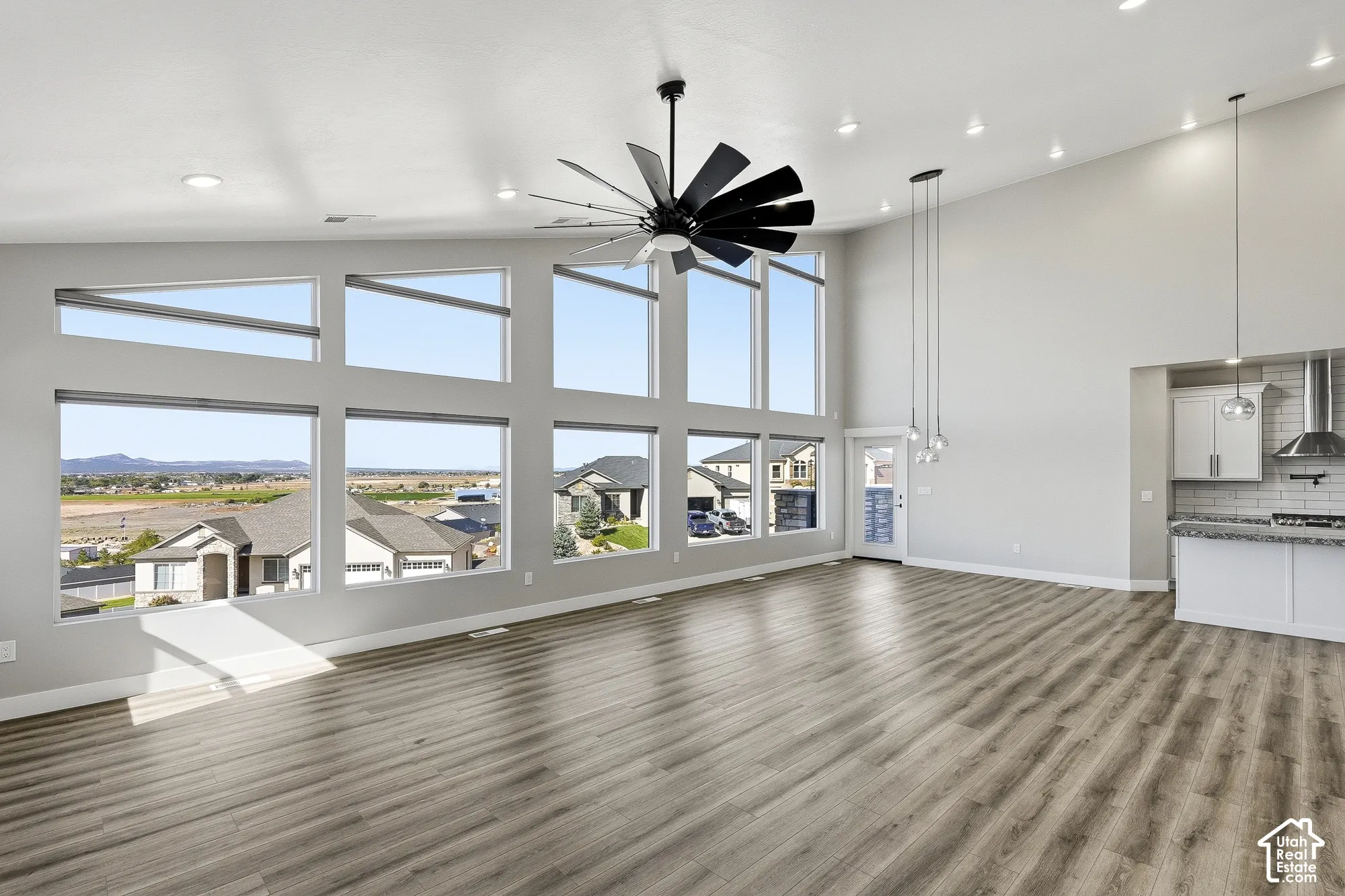 Vaulted ceiling with recessed lighting, large picture windows, wood-finish flooring, contemporary ceiling fan, and pendant lighting fixtures