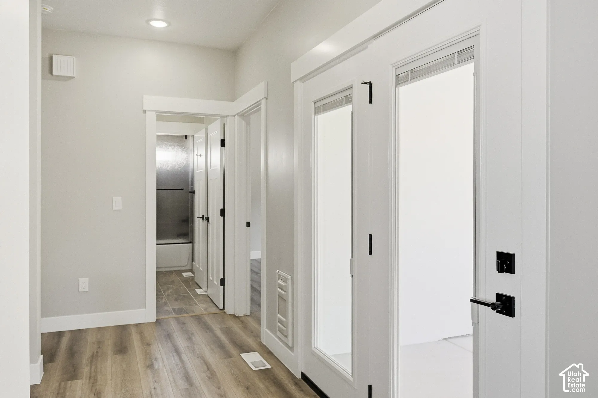 Wood-finish flooring throughout, bright white walls, recessed ceiling lighting, and matte black door hardware
