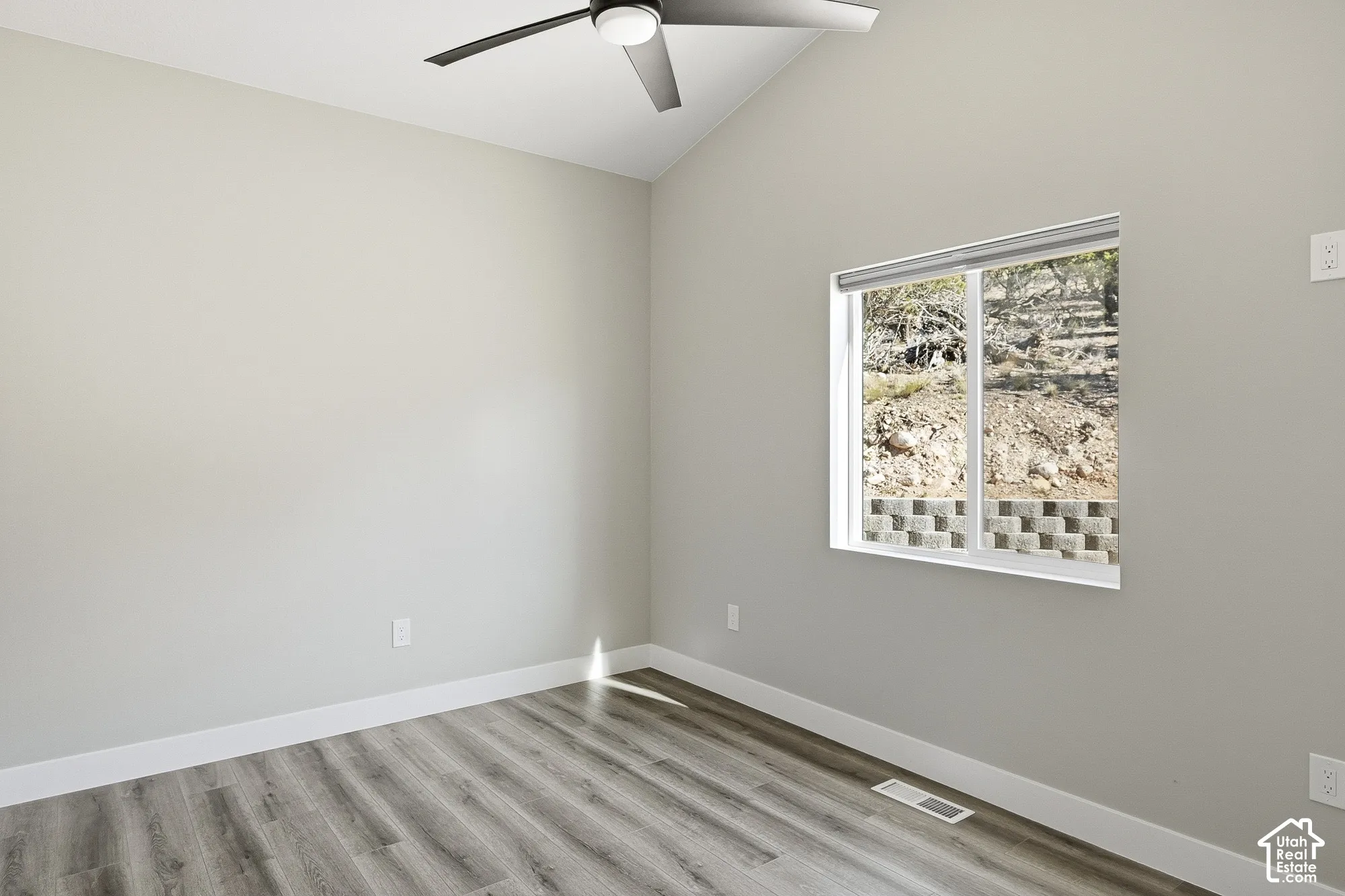 Wood-finish flooring with white trim, vaulted ceiling, and a modern ceiling fan