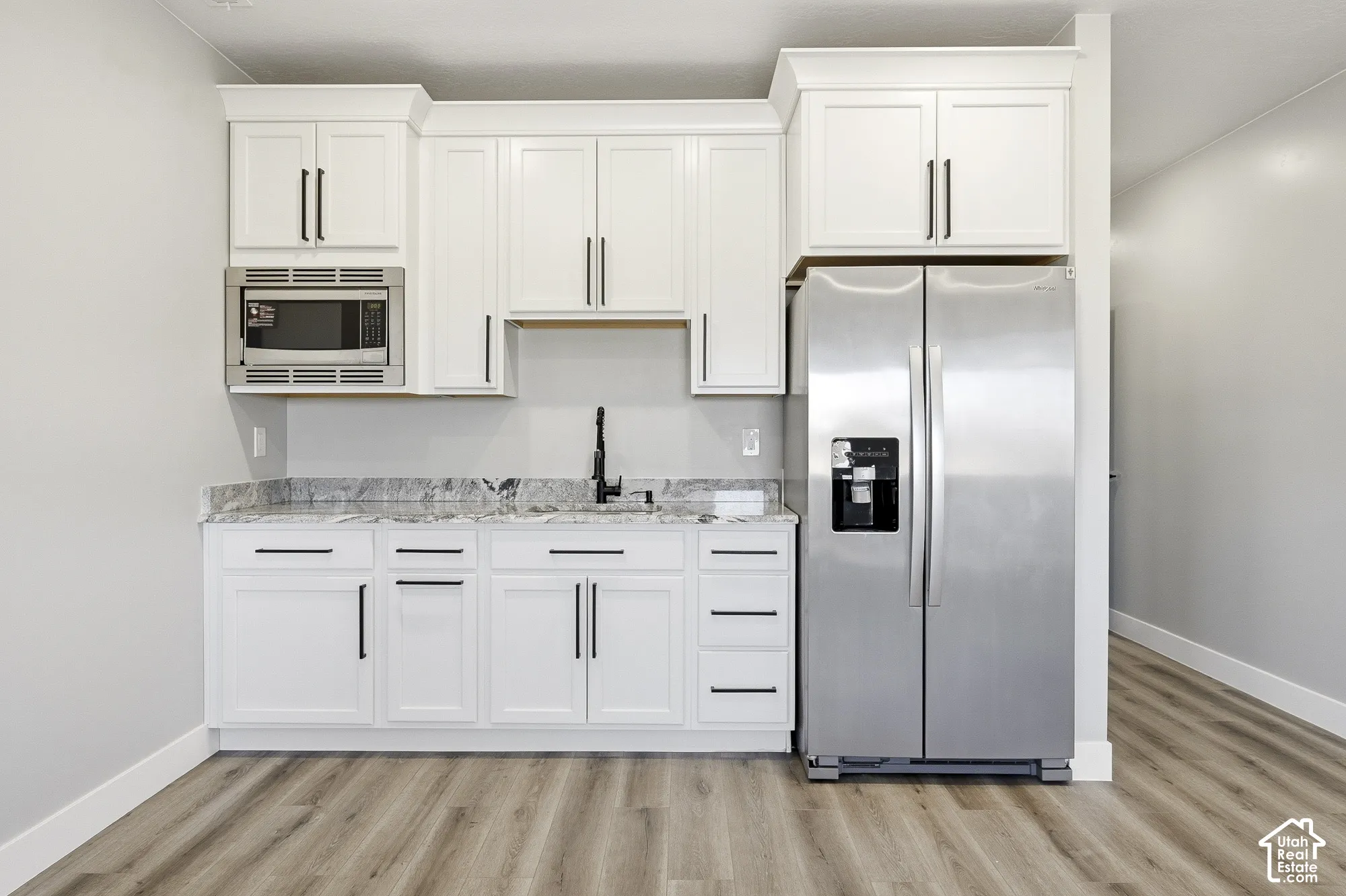 White cabinetry with dark hardware, stainless steel refrigerator, built-in microwave, dark faucet, and wood-finish flooring