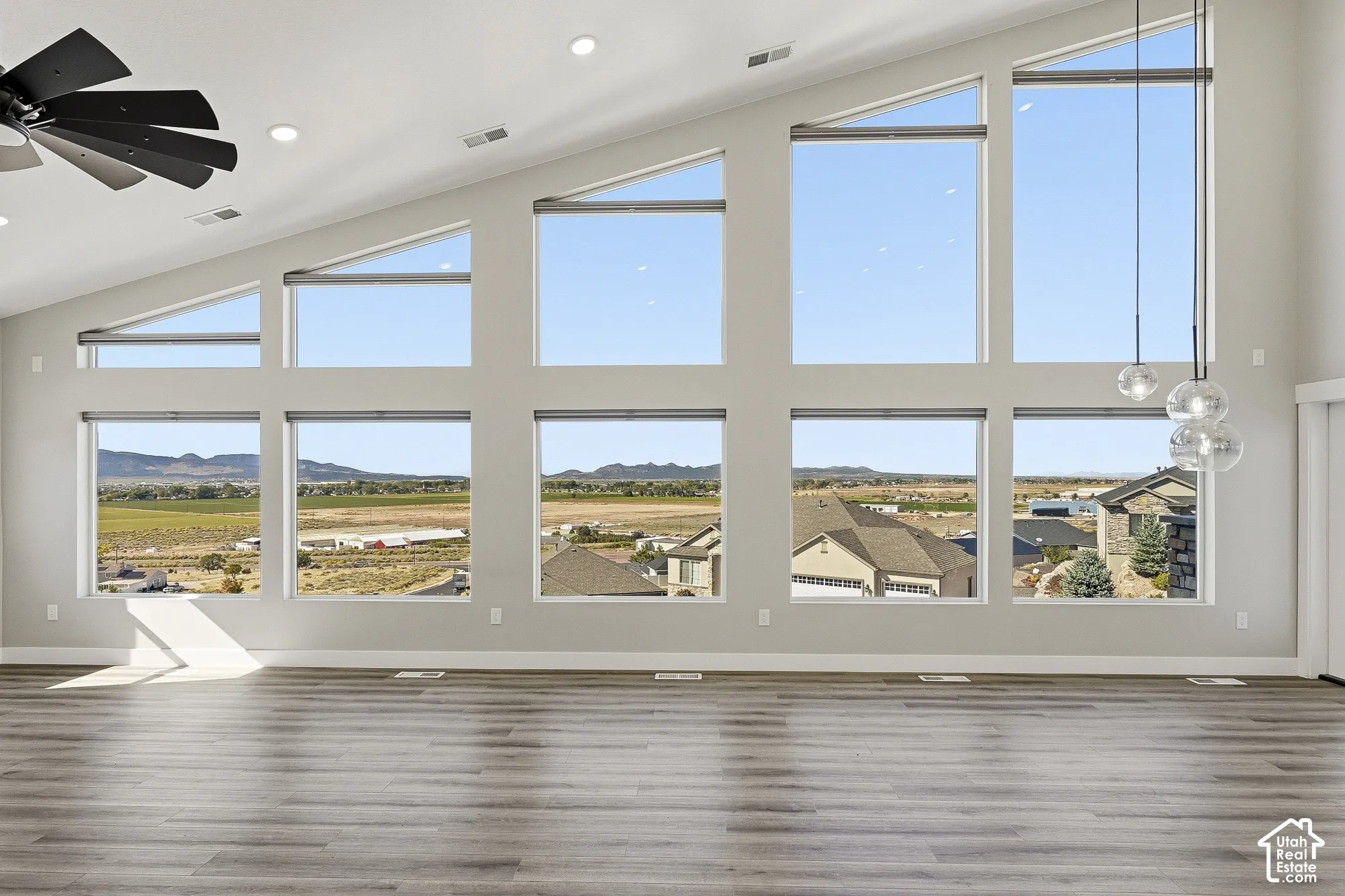 Vaulted ceiling with recessed lighting, expansive multi-pane windows, wood-finish flooring, contemporary ceiling fan, and pendant light fixture