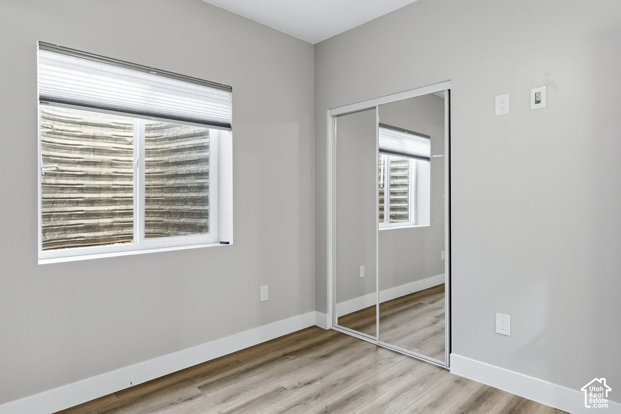 Light gray walls with white trim, wood-finish flooring, and a mirrored sliding closet door