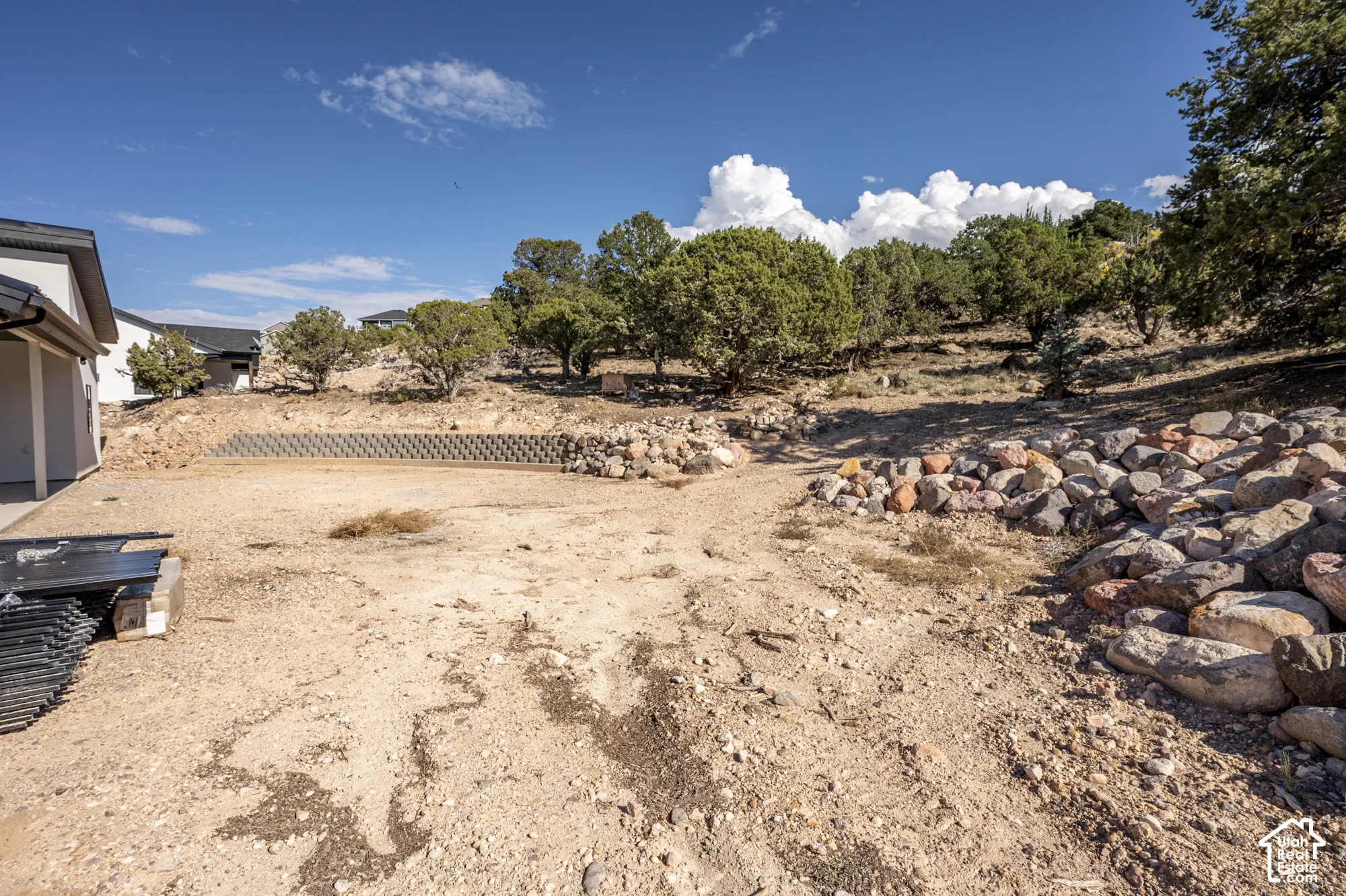 Graded lot with a concrete retaining wall, natural rock landscaping, and mature trees on the surrounding terrain