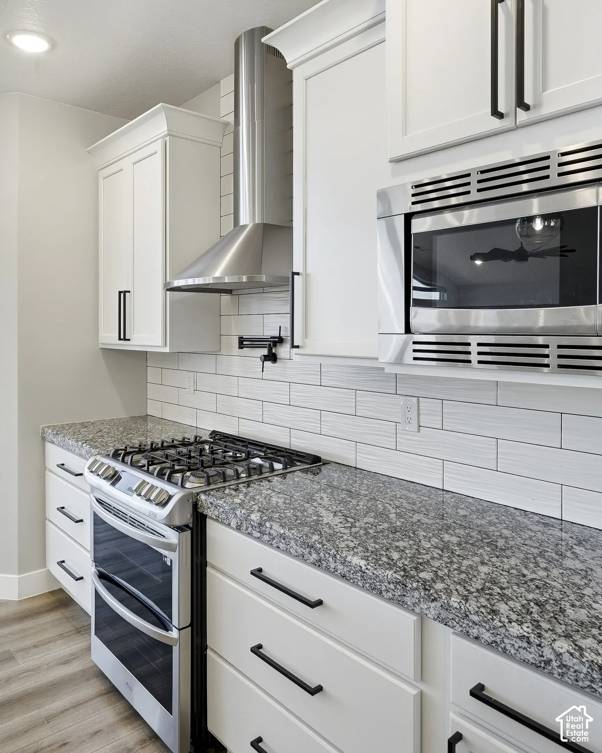 White shaker-style cabinetry with matte black hardware, stainless steel gas range with double oven, stainless steel microwave, stone countertops, and white subway tile backsplash