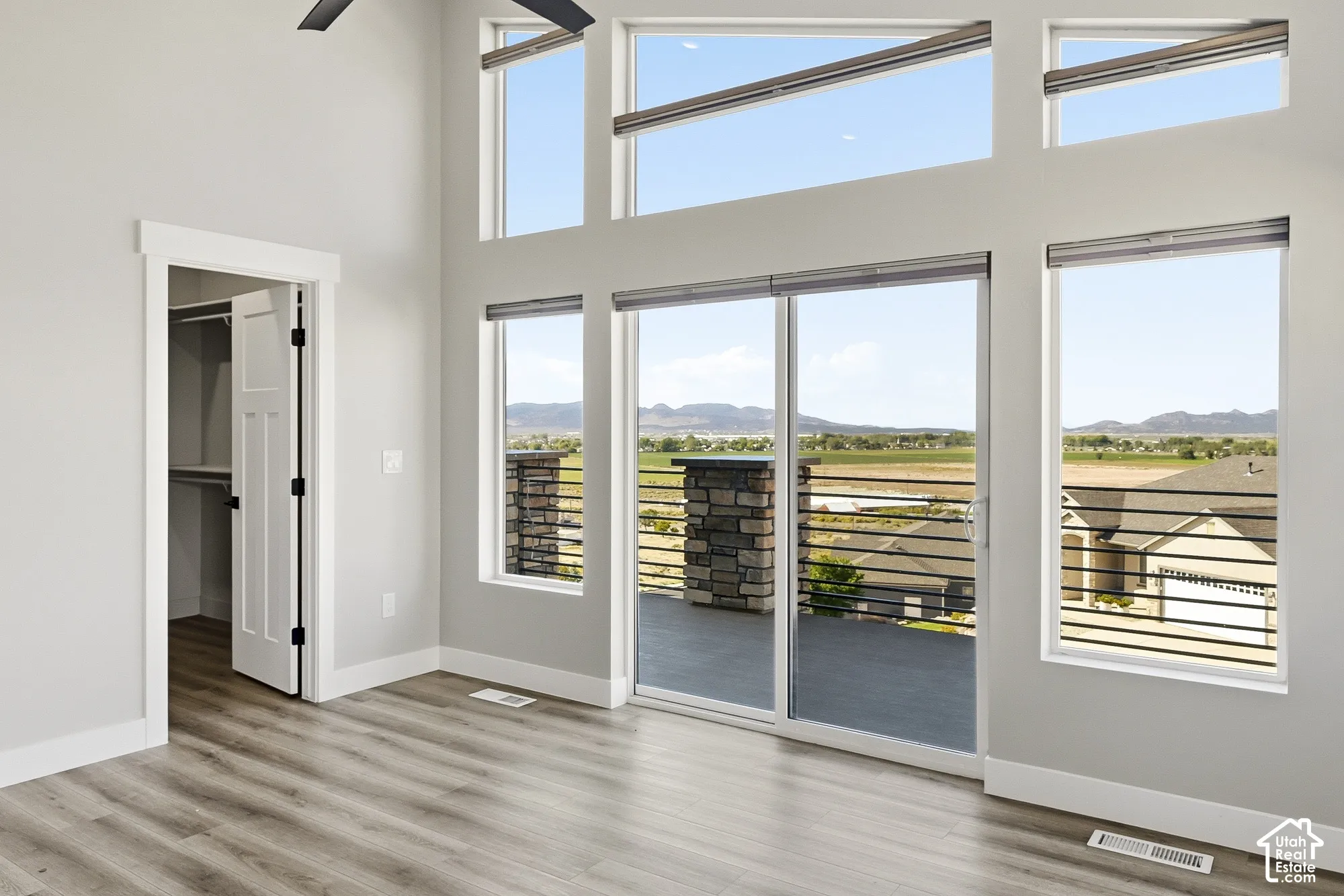 Vaulted ceilings with clerestory windows, wood-finish flooring, sliding glass door, built-in closet shelving, and a dark-toned ceiling fan